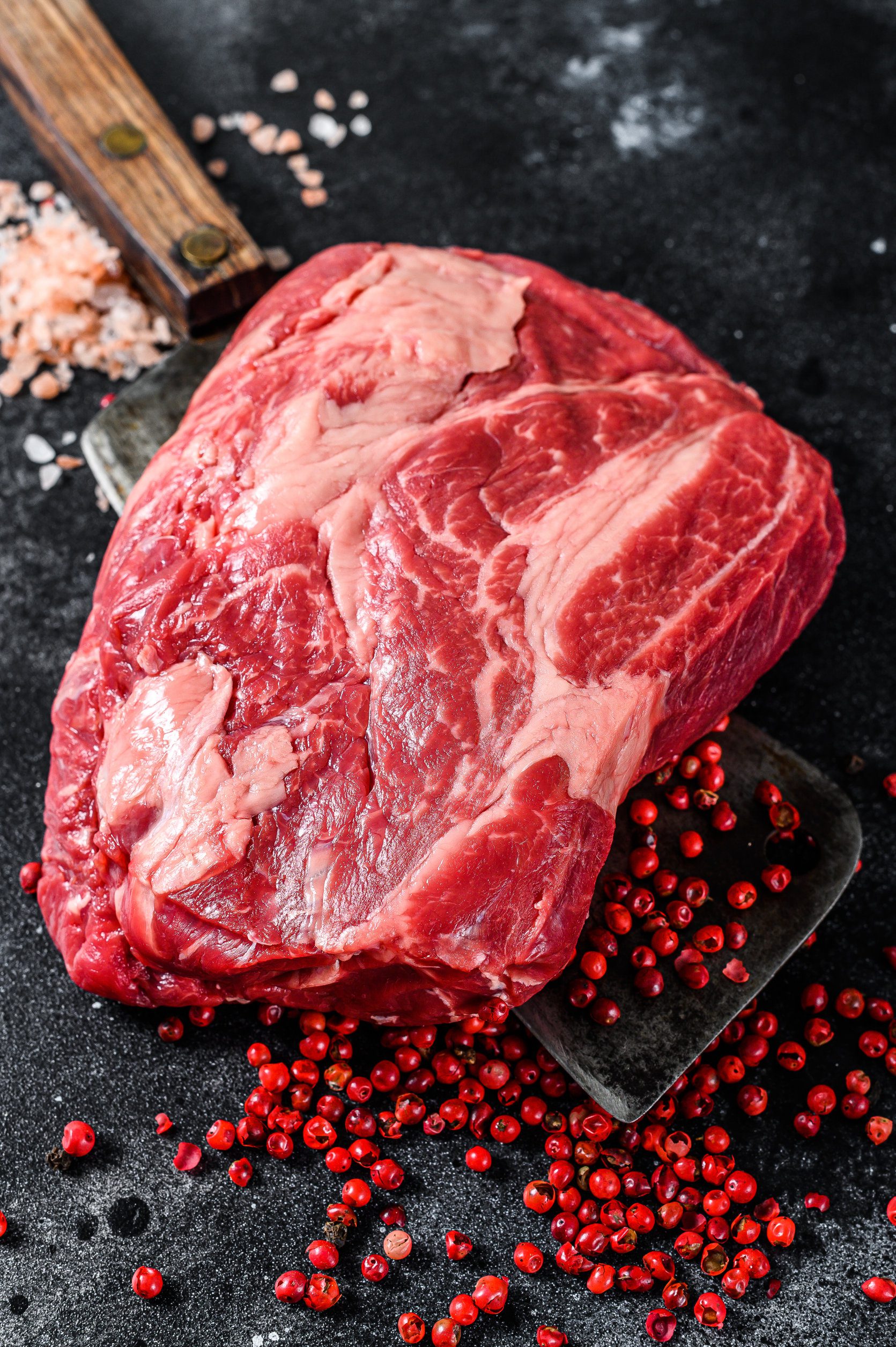 Fresh raw beef marbled steak. Chuck eye roll on a cleaver. Black background. Top view Fresh raw beef marbled steak. Chuck eye roll on a cleaver. Black background. Top view.